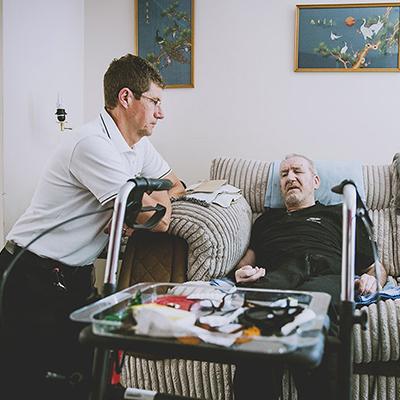 A young man is listening to an older man who is sat on a couch